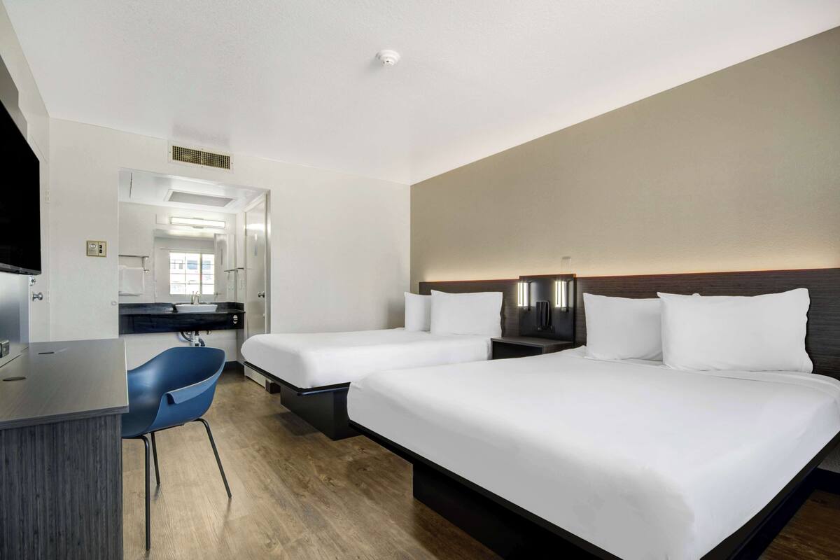 Une chambre d’hôtel avec deux lits, un bureau, une chaise, une télévision et une salle de bain visible à travers une porte ouverte.