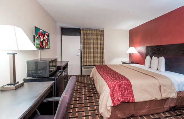 A hotel room with a bed, a desk, a television, a lamp, and a patterned carpet.