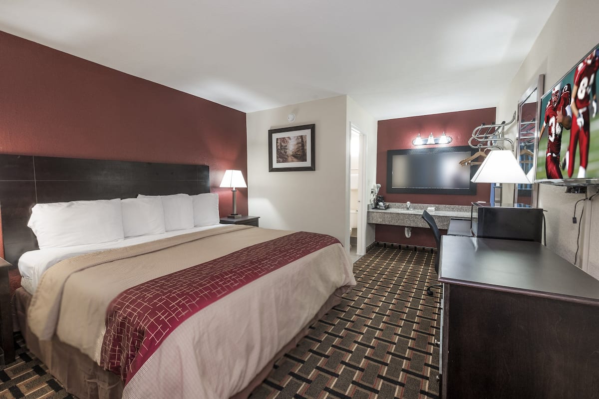 Une chambre d’hôtel avec un lit, un bureau, une télévision et une salle de bain visible à travers une porte ouverte.