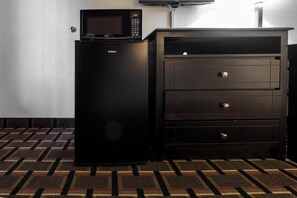 A black refrigerator with a digital display and a microwave above it, next to a dark wooden dresser with drawers.