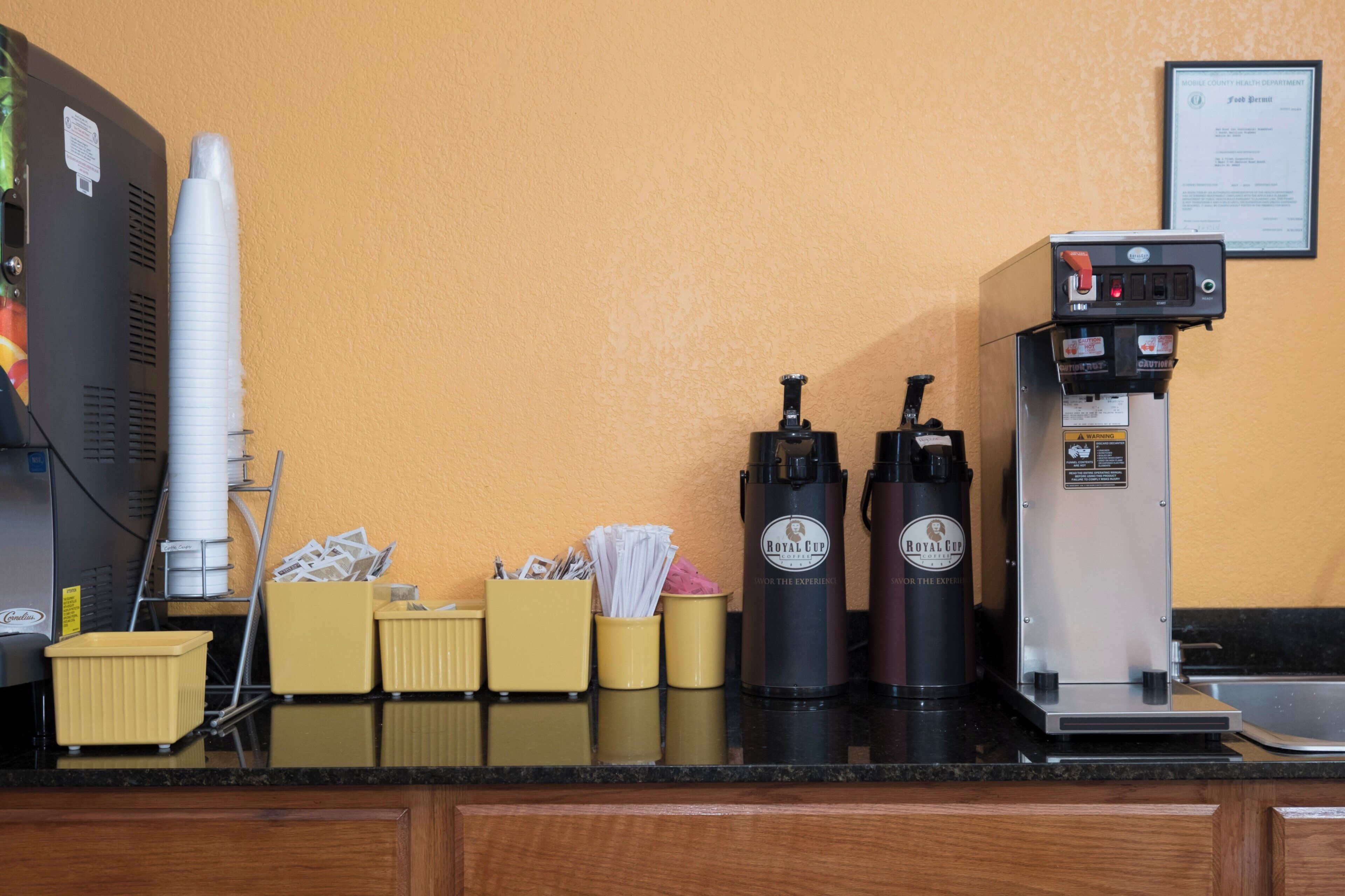 A coffee station with a coffee machine, two dispensers, and paper cups.