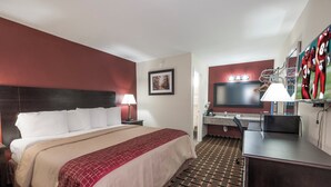A hotel room with a bed, desk, TV, and a red wall.