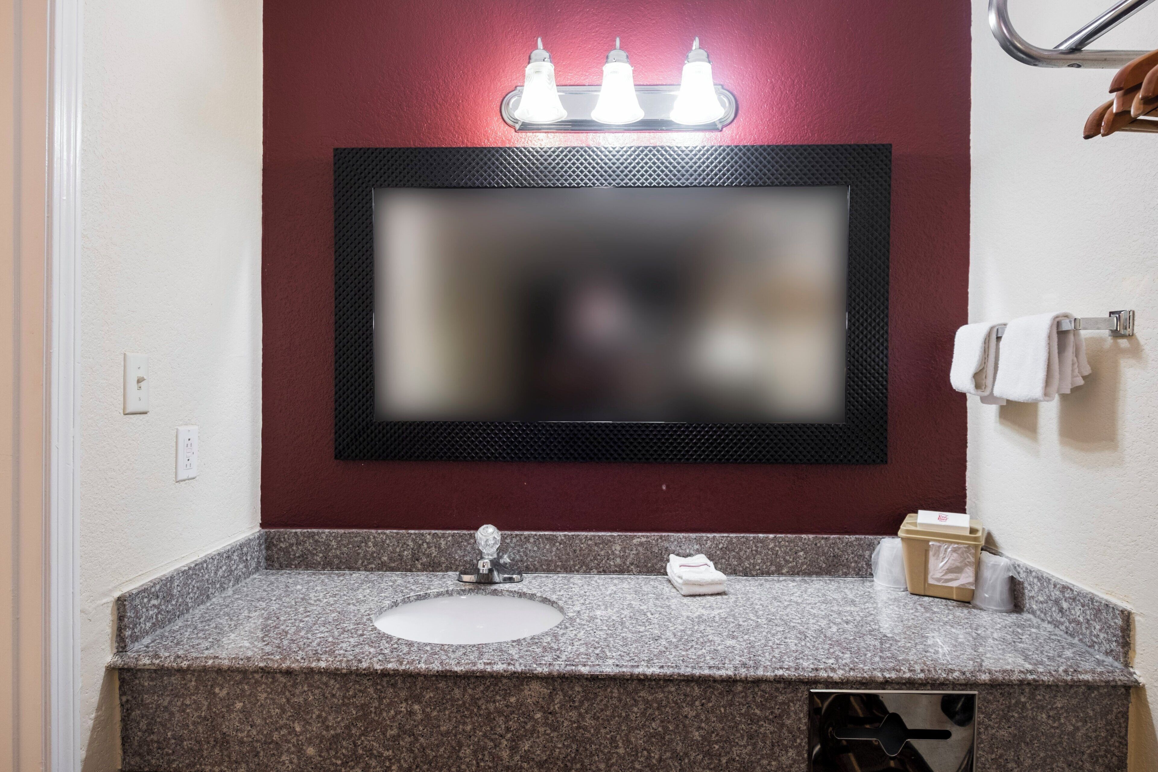 Un baño con encimera de granito, un lavabo blanco, un espejo con marco negro y un perchero con toalla blanca.