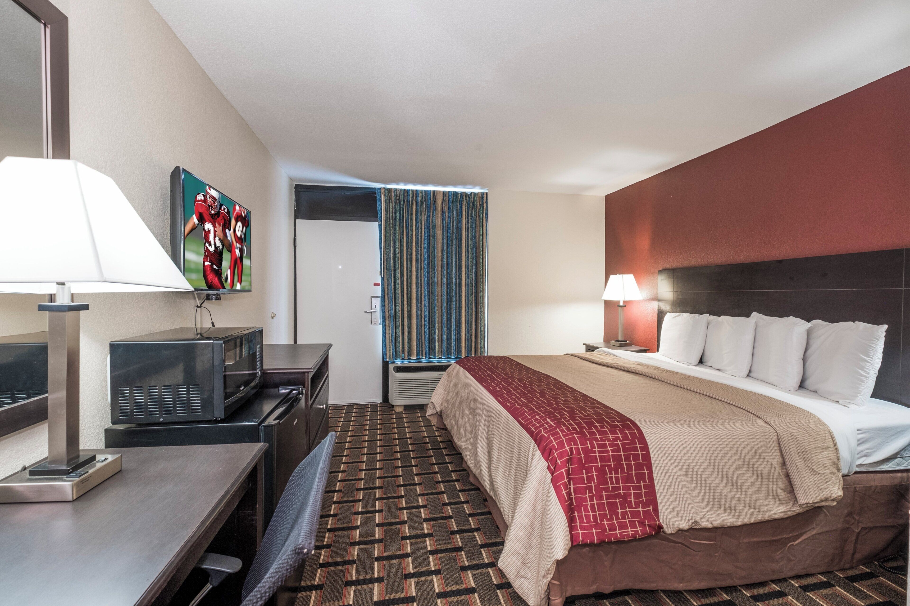 Una habitación de hotel con una cama, un escritorio con lámpara, un televisor y un microondas.