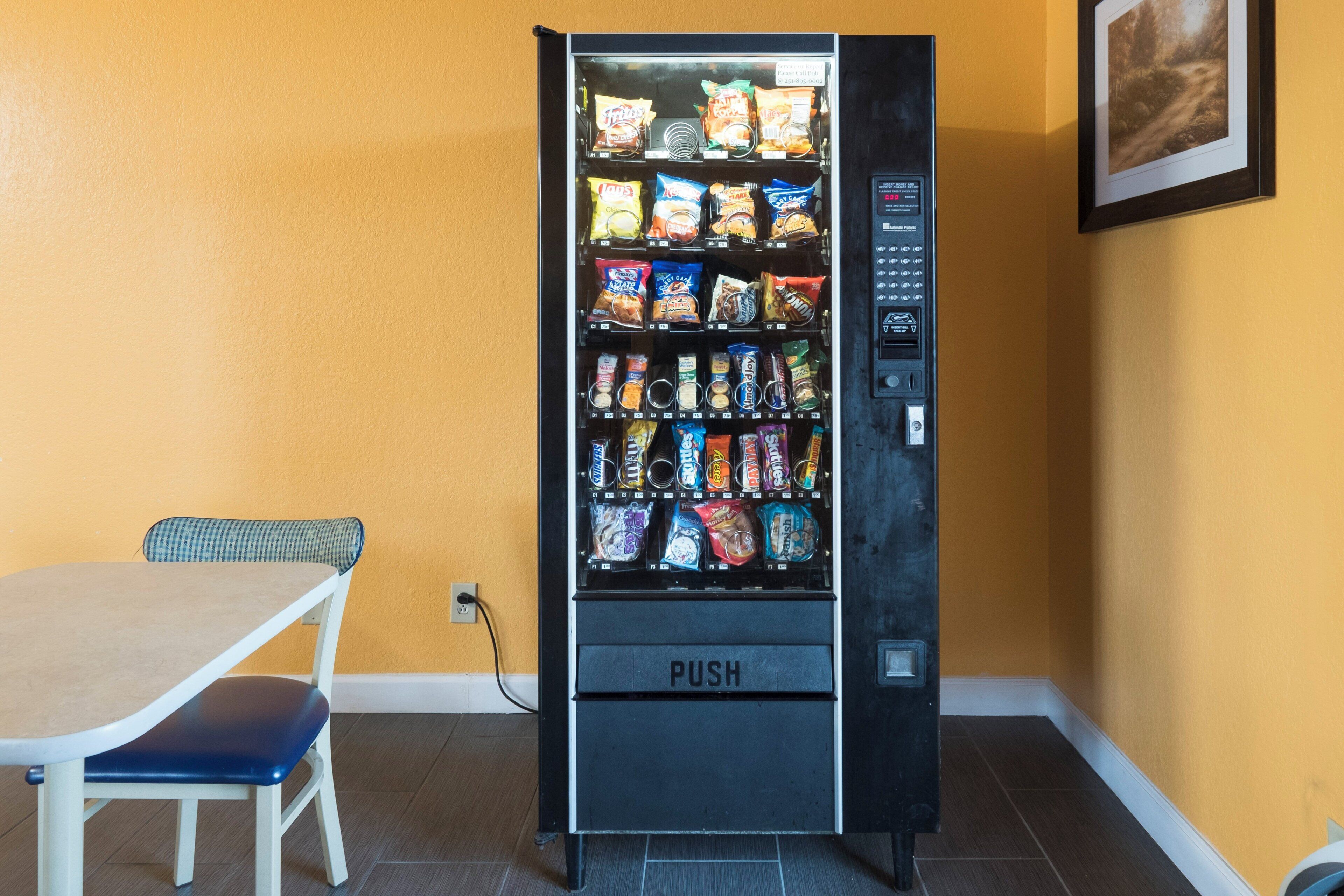 A vending machine with a variety of snacks and drinks, located next to a table and chair.