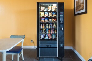 Una máquina expendedora con diferentes refrigerios y bebidas, ubicada junto a una mesa y una silla.