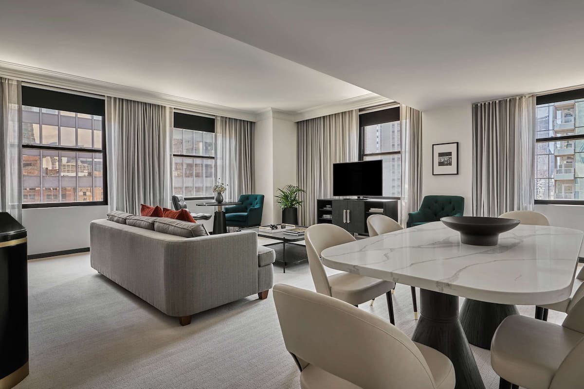 A modern living room with a sofa, a dining table with chairs, a TV, and large windows with curtains.