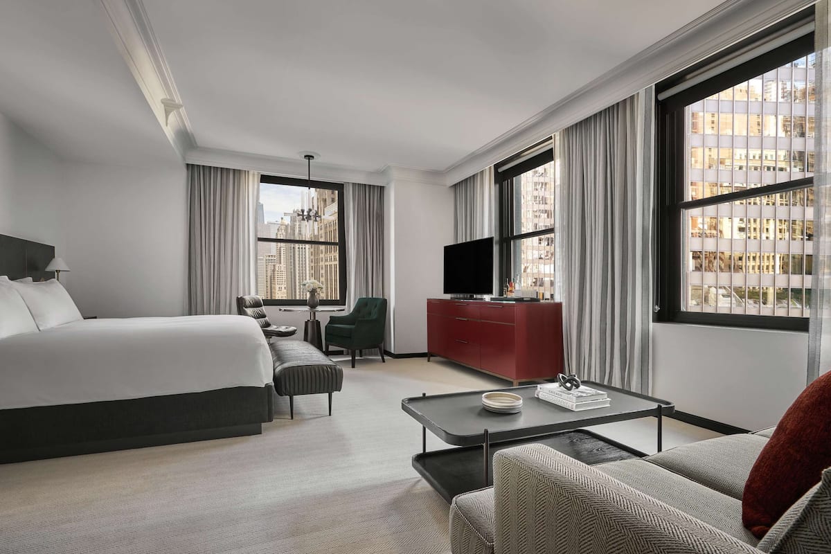 A hotel room with a large bed, a sofa, a TV, a red cabinet, and a city view.