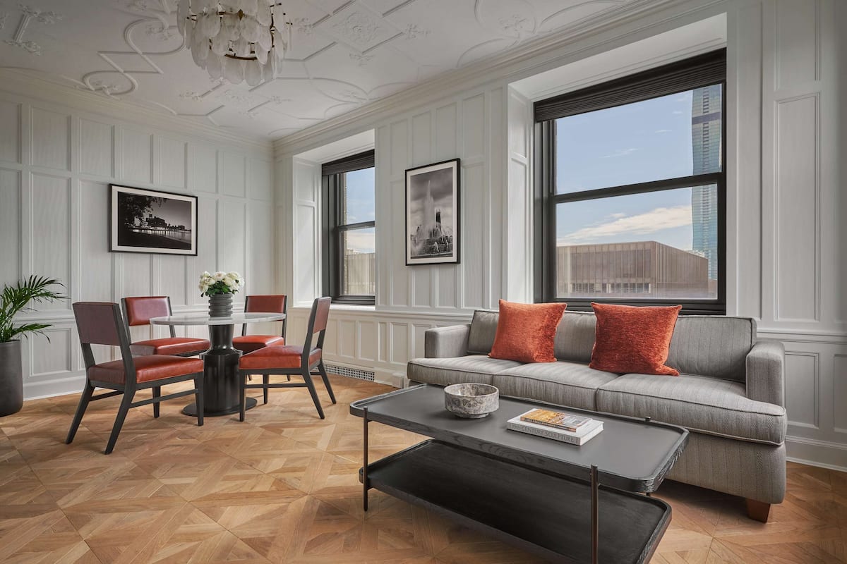 A spacious living room with a grey sofa, red and black chairs, a coffee table, and a large window with a city view.