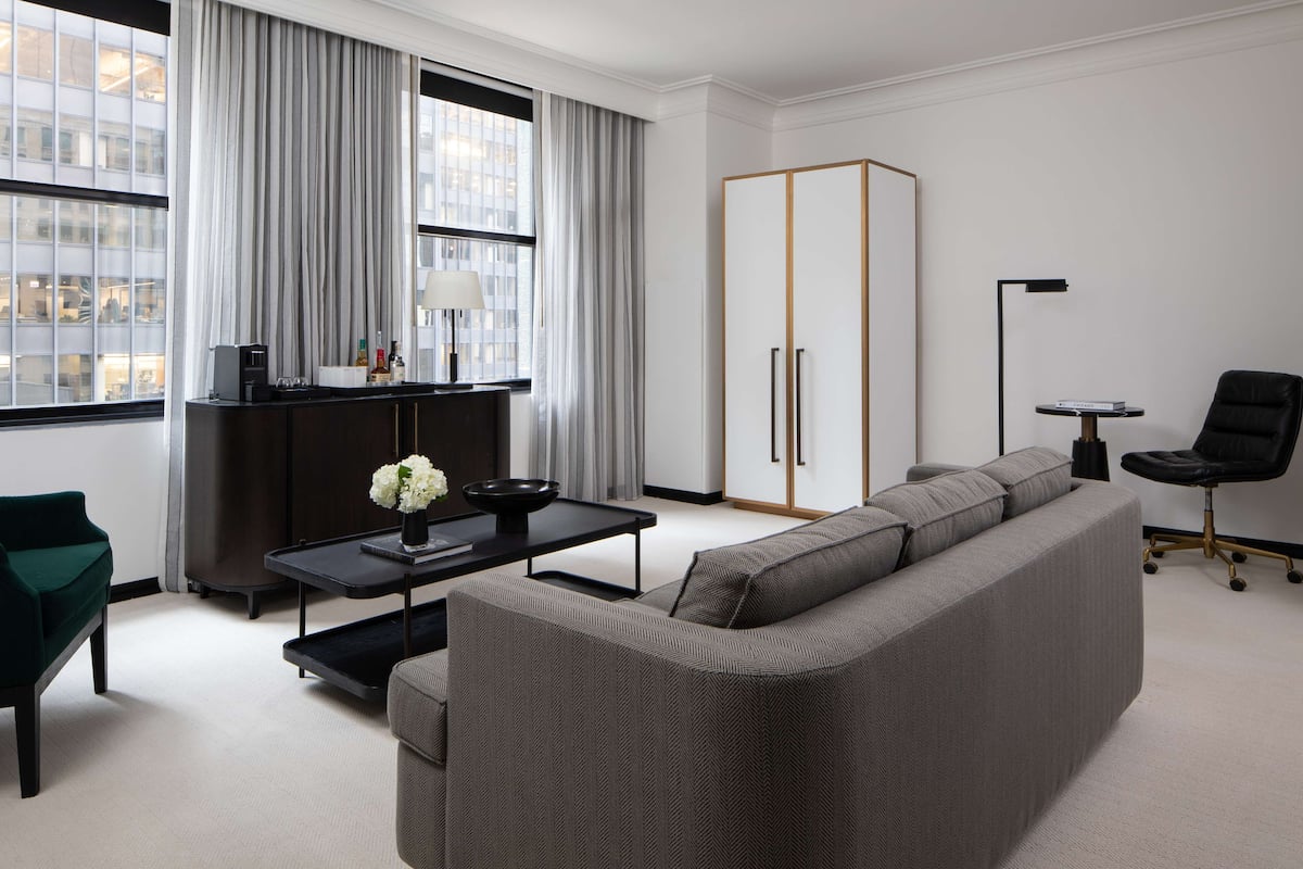 A modern living room with a grey sofa, a dark wooden side table, a green chair, a black office chair, and a wardrobe with two doors.