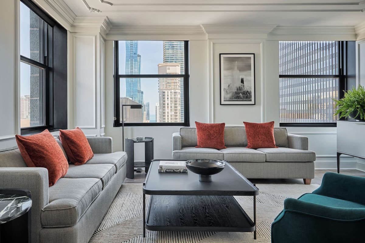 A modern living room with a grey sofa, a black coffee table, and a view of the city skyline through large windows.