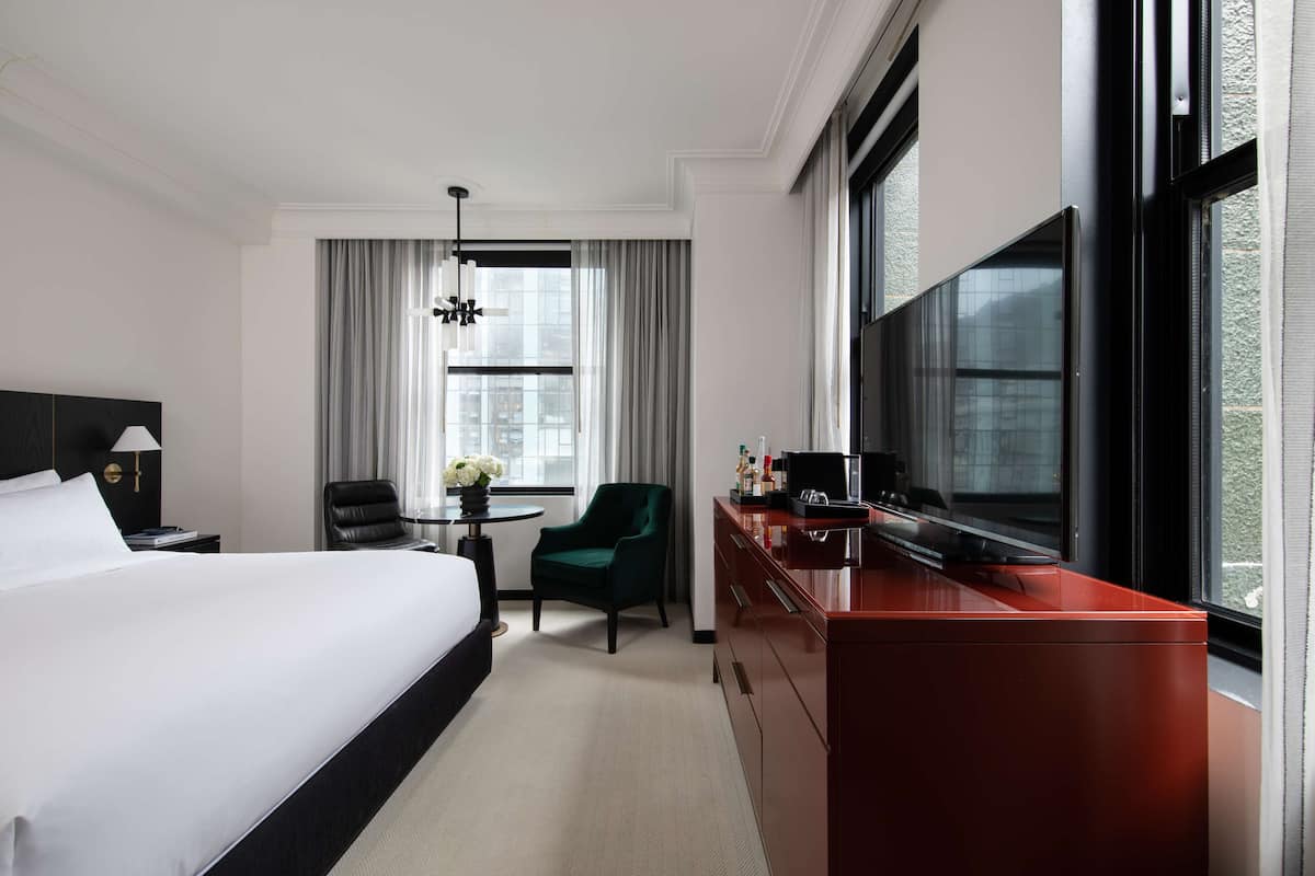 A hotel room with a large bed, a desk with a TV, a chair, and a window with curtains.