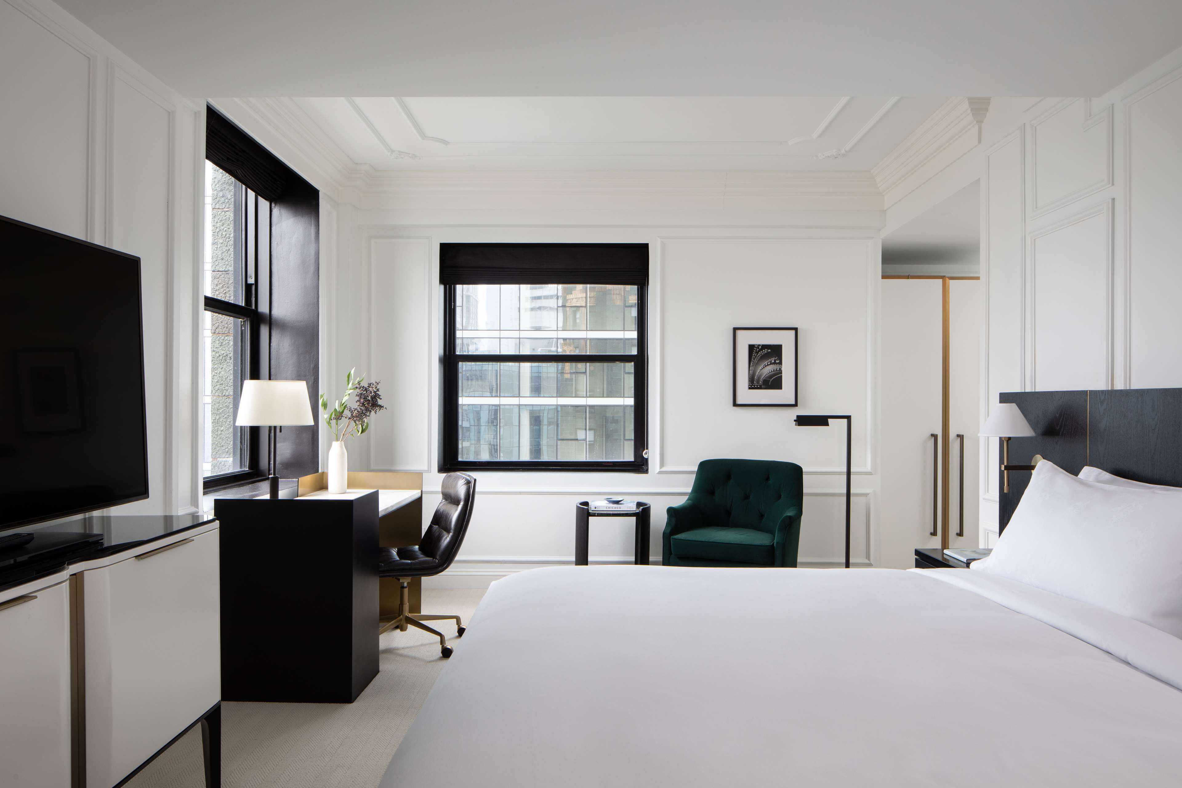 Habitación de hotel con una cama grande, un escritorio, una silla, un televisor, una ventana y una lámpara.