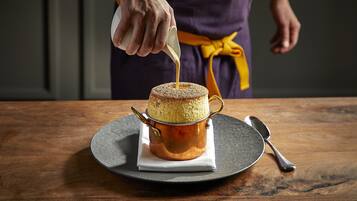 Un gâteau dans un récipient en cuivre, posé sur une table en bois, avec une cuillère et une serviette à proximité.
