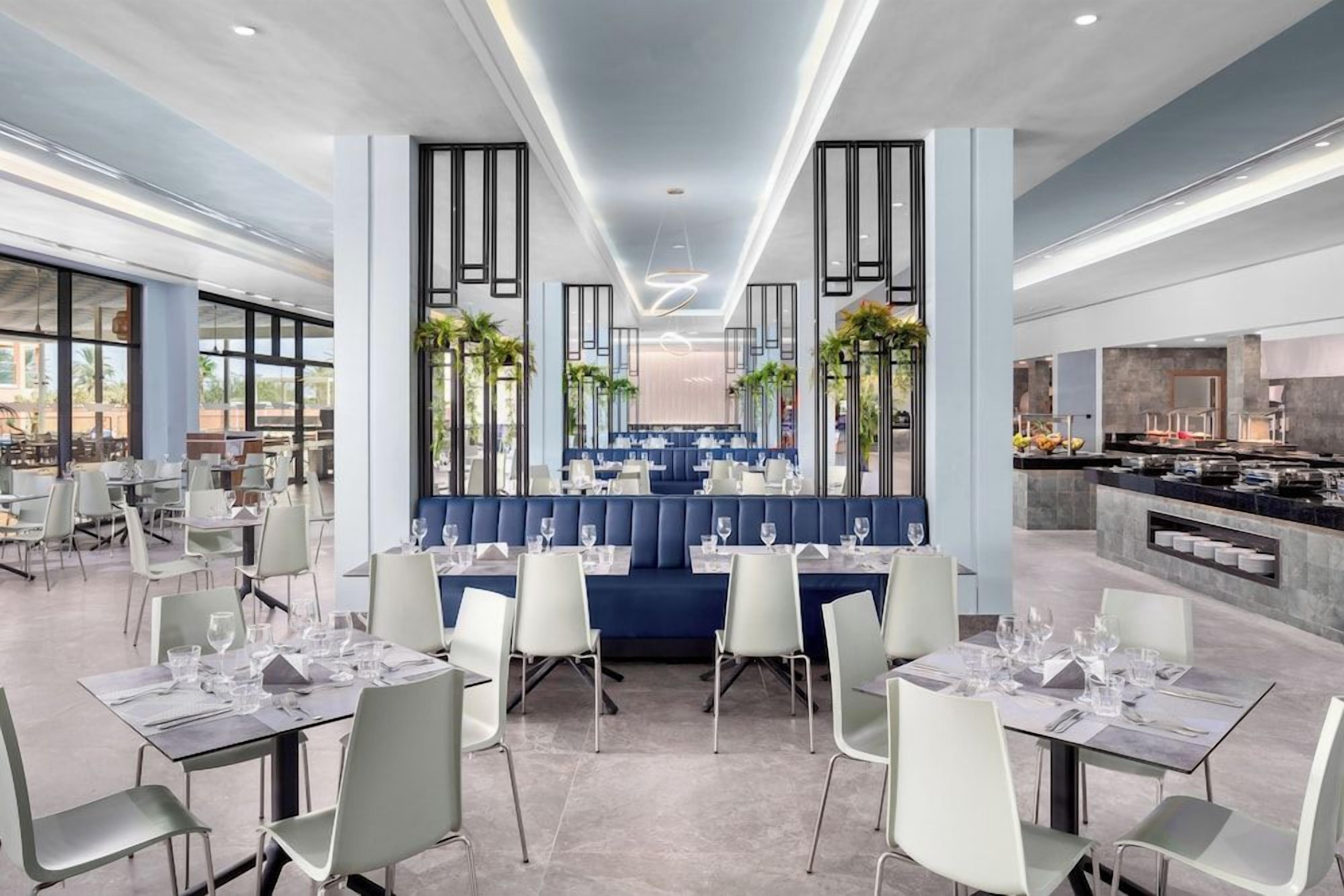 Ein modernes Restaurant mit einer zentralen Sitzgruppe, hohen Decken und Blick auf die Stadtlandschaft.