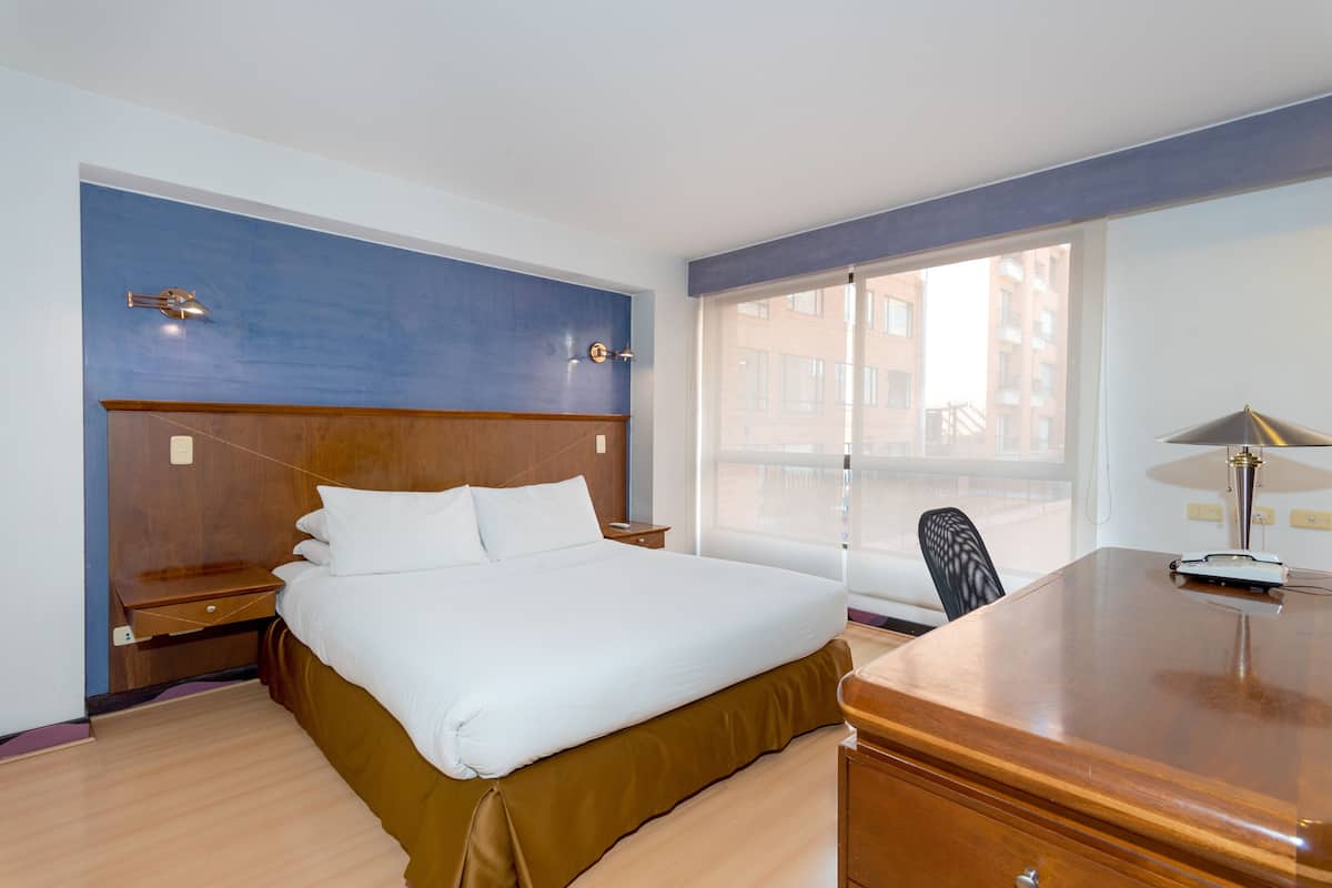 Camera d'albergo con un letto grande, una scrivania, una sedia e una finestra che dà su edifici.