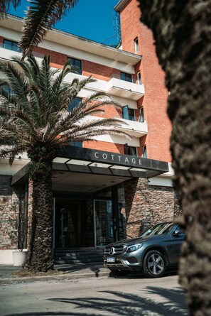 A building with a sign reading "COTTAGE" above the entrance, a parked car, and a palm tree in front.