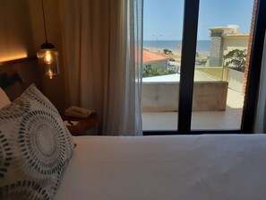 A hotel room with a bed, a bedside telephone, a decorative pillow, and a view of the beach and ocean through large windows.