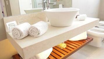 Un baño moderno con un lavamanos grande de color blanco, dos toallas enrolladas sobre la encimera y un estante de madera debajo.