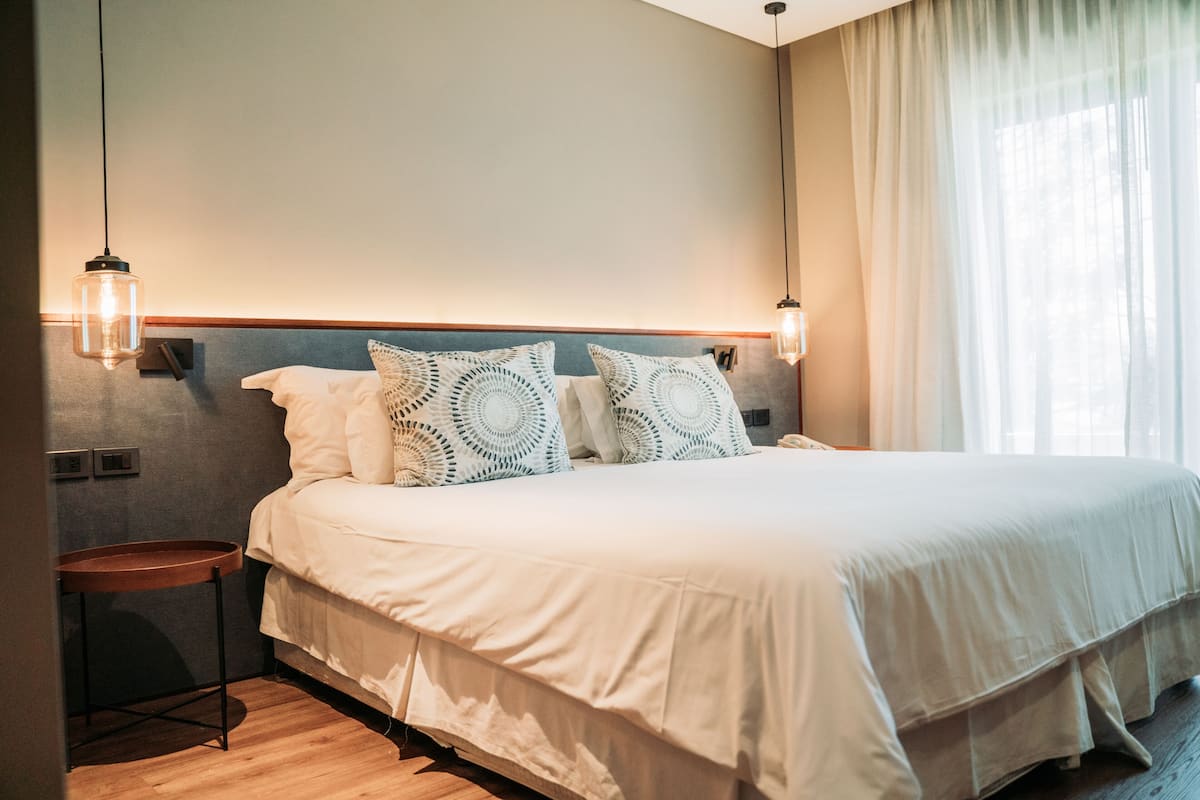 A neatly made bed with a wooden headboard, two bedside tables, and a large window with sheer curtains.
