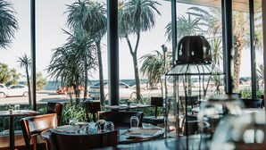 Un ristorante con ampie vetrate, tavoli, sedie e un lampadario.