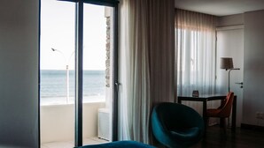 Camera d'hotel con un letto, una sedia, un tavolo e vista sul mare attraverso un'ampia finestra.