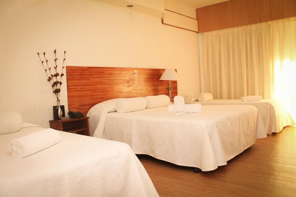 Ein Hotelzimmer mit zwei Betten, einem Holz-Kopfteil, einem Nachttisch mit Lampe und einer Zimmerpflanze.
