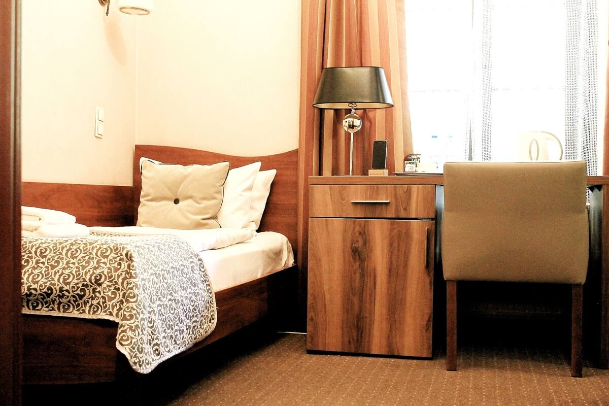 A hotel room with a bed, a desk, a chair, a lamp, and a wardrobe.