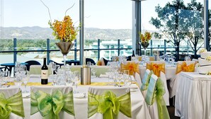 Un salón de banquetes con mesas dispuestas para un evento formal, destacando centros de mesa florales y sillas con cintas decorativas.