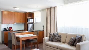 A modern living room with a beige sofa, patterned cushions, and a dining area with wooden furniture.