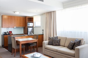 A modern living room with a beige sofa, patterned cushions, and a dining area with wooden furniture.