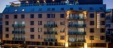 A multi-story hotel with a distinctive curved roof, balconies, and a well-lit outdoor area with umbrellas.