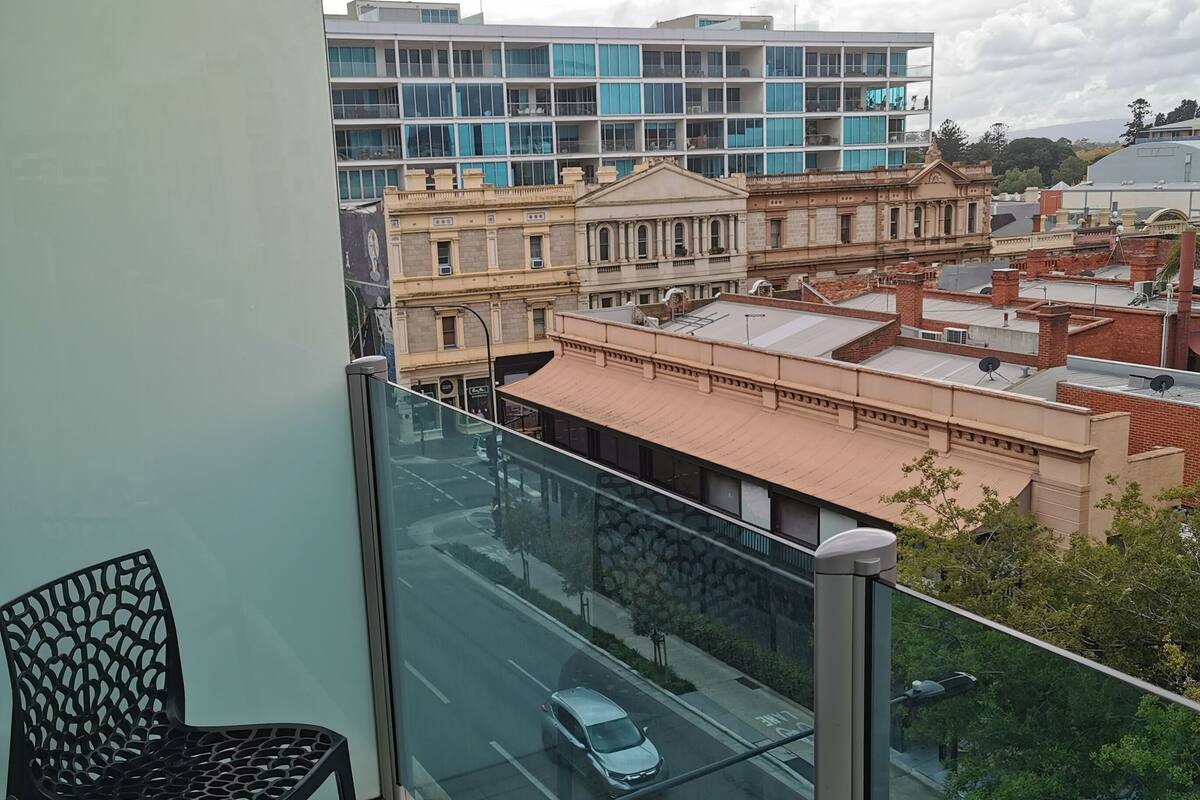 Un balcón con vista a una calle de la ciudad, un coche aparcado y edificios al fondo.