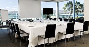 Un salón de conferencias con una gran mesa, sillas, una pantalla y vistas a la ciudad.