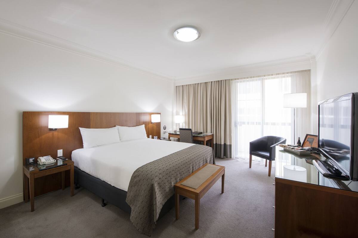 Una habitación de hotel con una cama grande, un escritorio, una silla, un televisor y una ventana con cortinas.