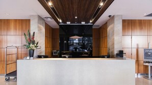 Un mostrador de recepción con diseño moderno, una pantalla digital que muestra el nombre del hotel y una planta a la izquierda.