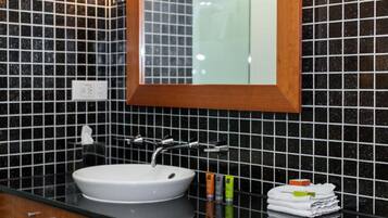 A bathroom with a white sink, black tiled walls, and a mirror with a wooden frame.