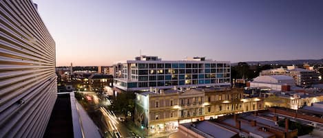 A modern building with a flat roof and large windows, surrounded by older buildings with traditional architecture.