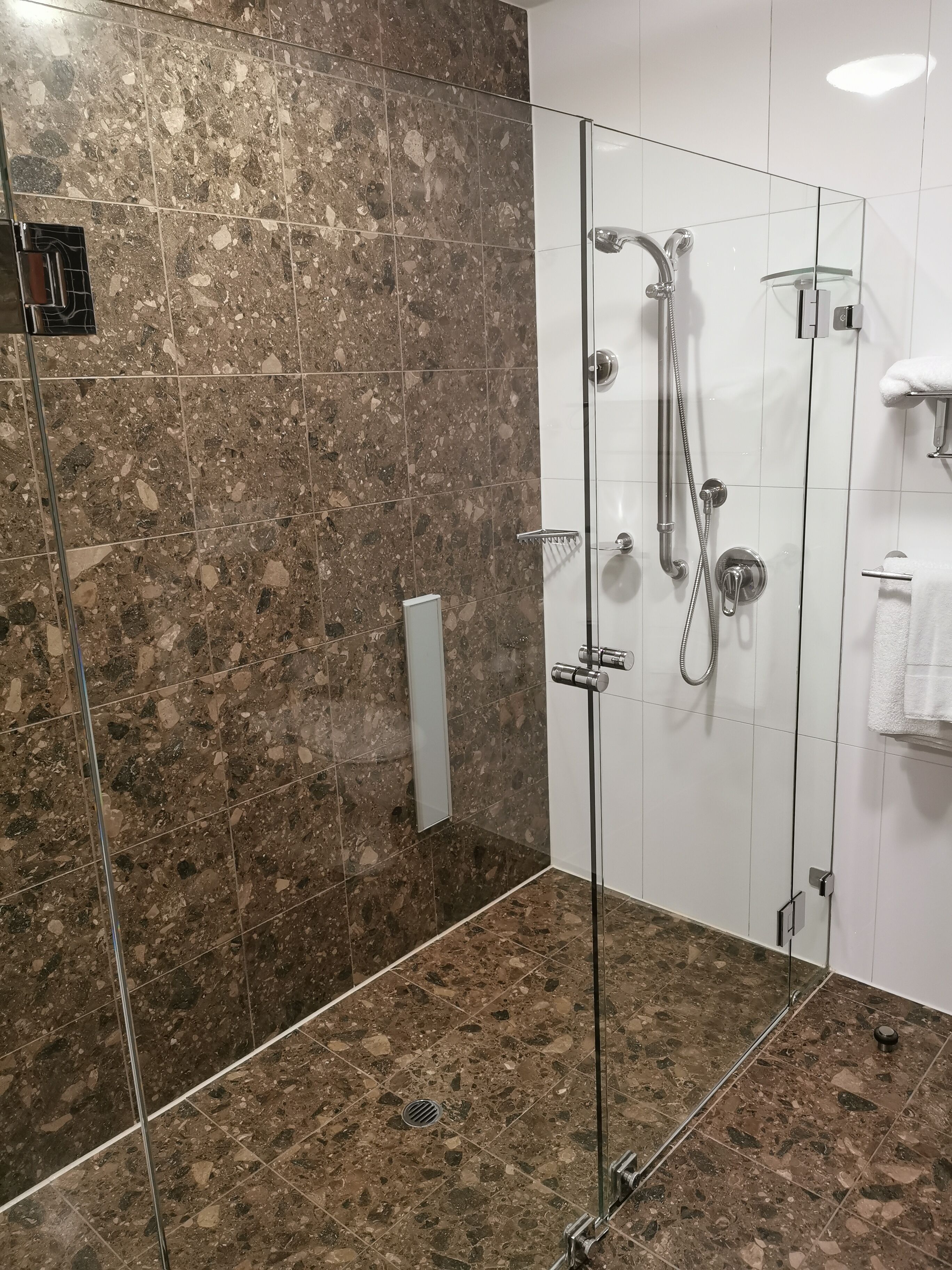 A modern bathroom with a glass-enclosed shower, marble tiles, and a white towel rack.