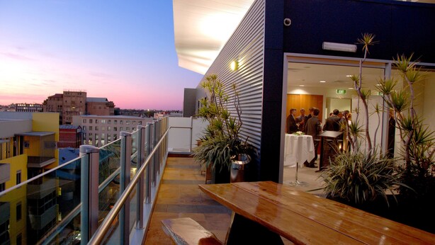 Terraza en la azotea con mesa y bancos de madera, plantas en macetas y vistas panorámicas de la ciudad.