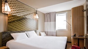 Ein Hotelzimmer mit einem großen Bett, einem Holzschrank, einem Schreibtisch mit einem Laptop und einem Fenster mit Vorhängen.
