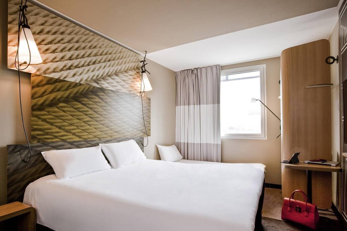 Een hotelkamer met een groot bed, een houten garderobe, een bureau met een laptop en een raam met gordijnen.