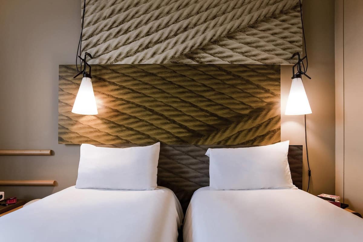 Een hotelkamer met twee bedden, een structuurwand en hanglampen.