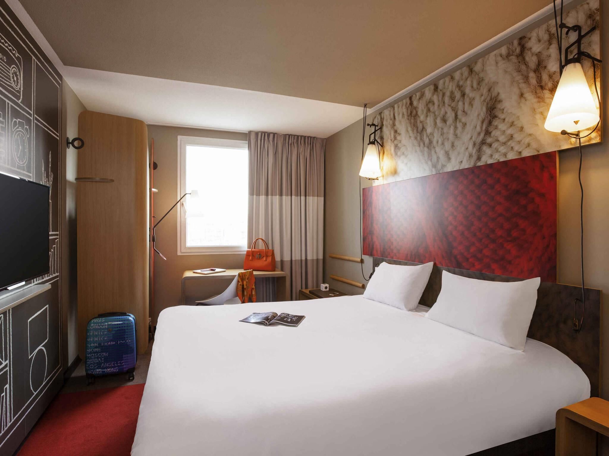 Ein Hotelzimmer mit einem großen Bett, einem Fernseher, einem Schreibtisch und einem fenster mit Vorhängen.