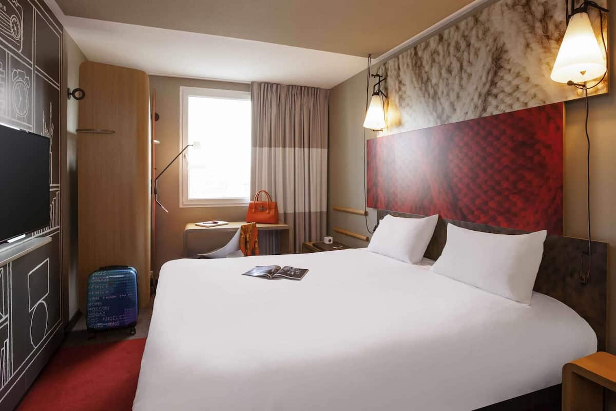 Ein Hotelzimmer mit einem großen Bett, einem Fernseher, einem Schreibtisch und einem fenster mit Vorhängen.