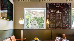 Interior de restaurante con sillas de cuero, una mesa con una bebida, un menú en la pared y una ventana con plantas afuera.