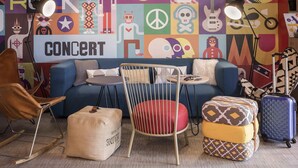 Una habitación con un sofá azul, una mesita redonda pequeña, una silla blanca, un sillón de cuero marrón y un reposapiés estampado.