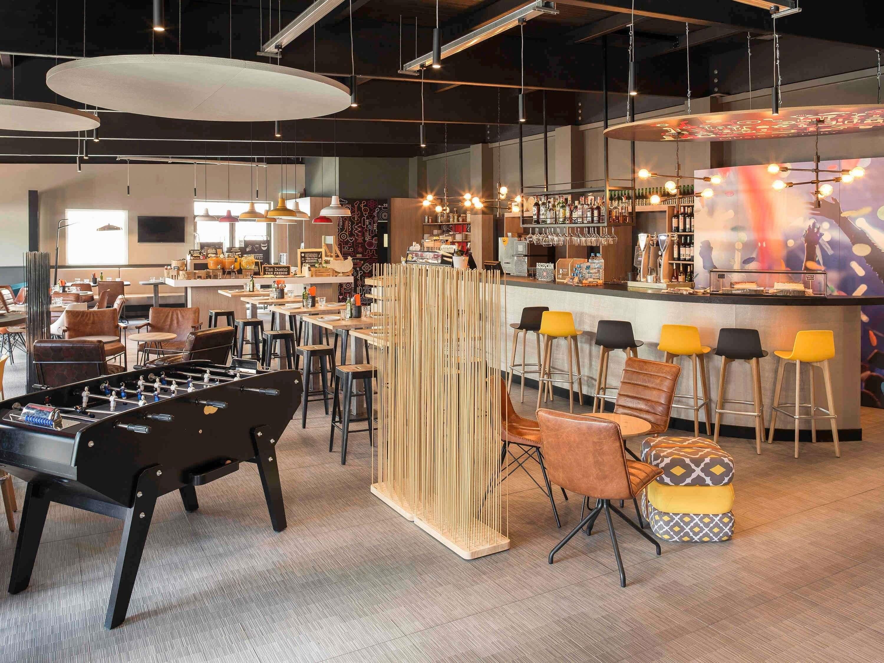 A modern bar area with stools, a foosball table, and a bar counter with a variety of bottles.