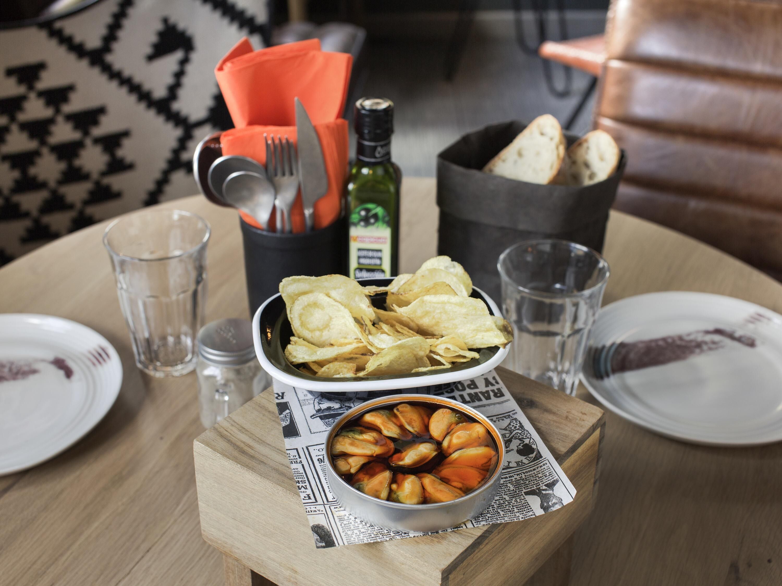 Une table à manger avec un bol de chips, un petit bol d’olives et une bouteille d’huile d’olive.