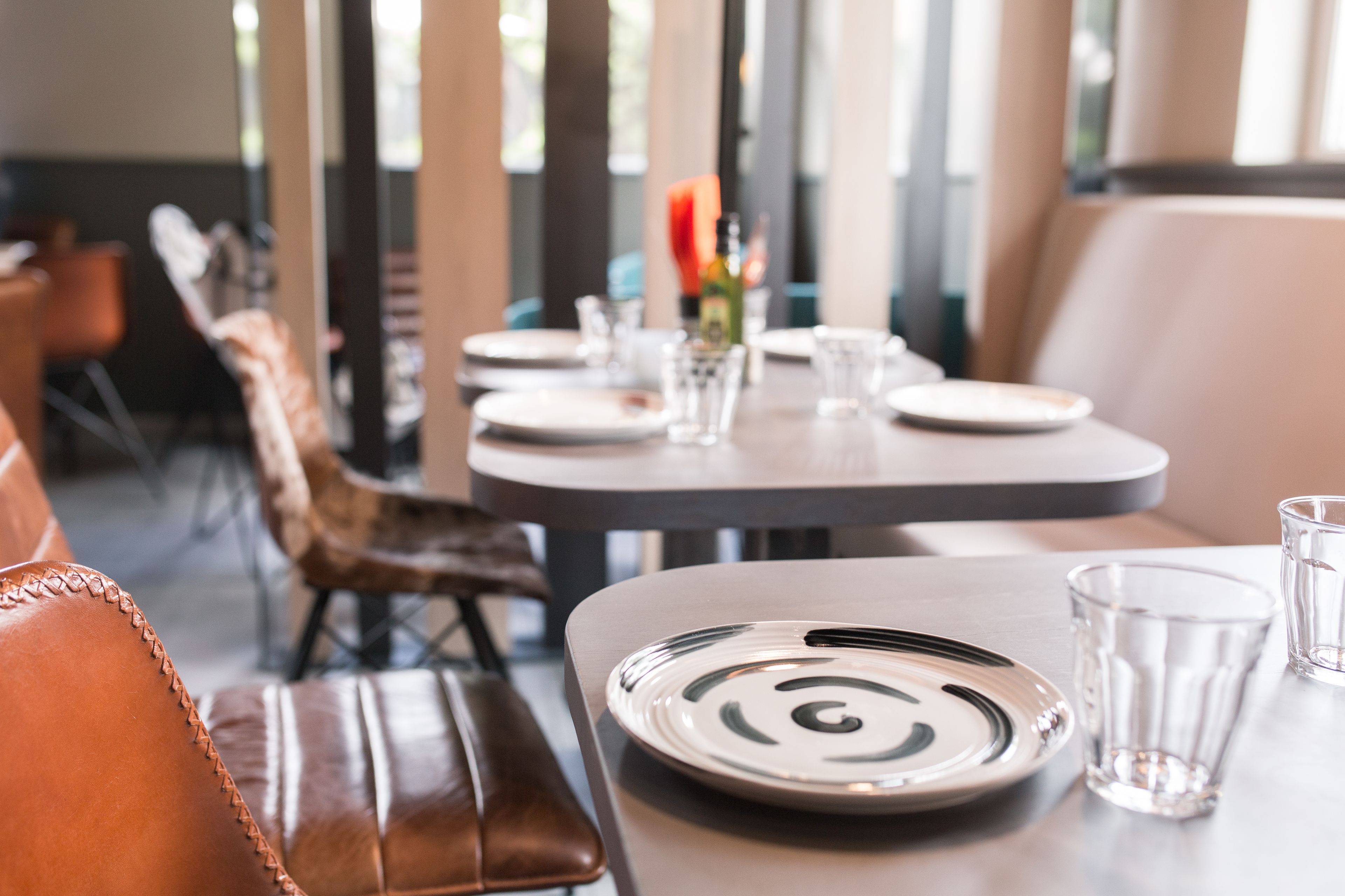 Un comedor con una mesa lista para dos personas, que incluye un plato con diseño en espiral, un vaso y una botella de agua.